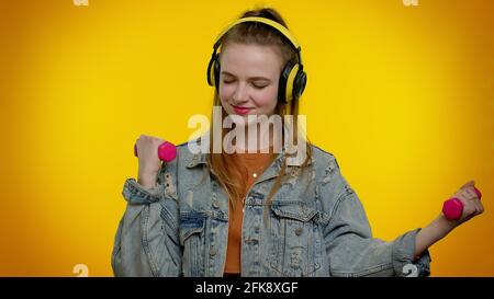 Ragazza studentesca sportiva che ascolta musica tramite cuffie, allenati, solleva i manubri sollevabili Foto Stock