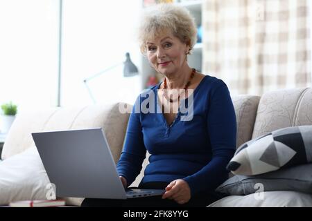 La donna anziana con il computer portatile è seduta sul divano Foto Stock