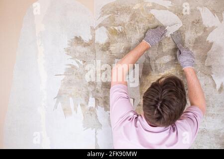 Processo di ristrutturazione degli appartamenti. Uomo caucasico strappando la vecchia carta da parati dalla parete che si prepara per la decorazione domestica Foto Stock