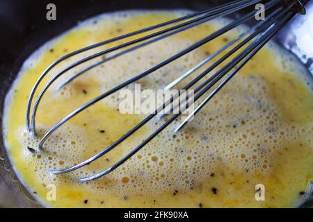 Primo piano di una frusta in un composto di uova, in un recipiente di vetro trasparente. Foto Stock
