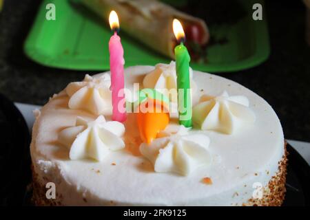 Primo piano di una torta di compleanno torta di carote, con due candele, e una carota di ghiaccio arancione sulla parte superiore. Foto Stock