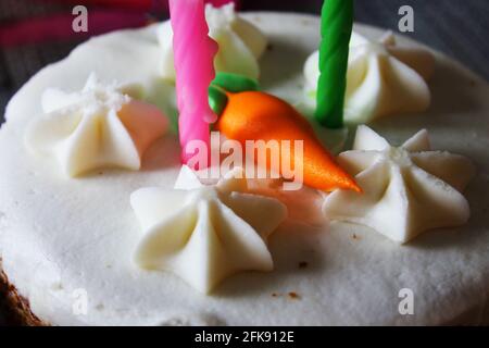 Primo piano di una torta di compleanno torta di carote, con due candele, e una carota di ghiaccio arancione sulla parte superiore. Foto Stock