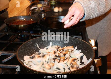 Primo piano di donna che aggiunge funghi ai funghi e cipolle in una padella. Foto Stock