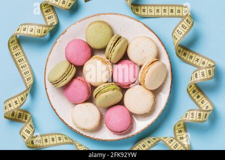 Piastra completa di macaron assortiti su sfondo blu con nastro di misurazione, vista dall'alto Foto Stock