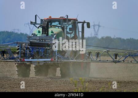 Trattore che spruzza campo di grano con spruzzatore, erbicidi e pesticidi. Spray con pesticida primaverile. Trattamento chimico agricolo. Foto Stock