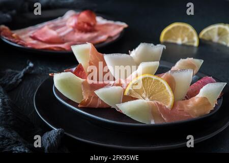 Melone di miele avvolto in prosciutto servito su un piatto nero Foto Stock