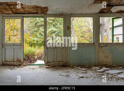 Casa abbandonata interno. Galleria con serramenti, vetri rotti e intonaco caduto, giardino d'autunno sopravorto visto attraverso le finestre Foto Stock