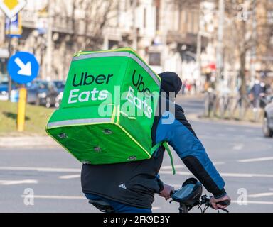 Bucarest, Romania - 03.17.2021: Uber mangia il corriere su una bicicletta che porta il sacchetto verde di consegna. Giovane adulto che consegna l'ordine Foto Stock