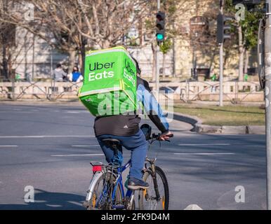 Bucarest, Romania - 03.17.2021: Uber mangia il corriere su una bicicletta che porta il sacchetto verde di consegna. Giovane adulto che consegna l'ordine Foto Stock