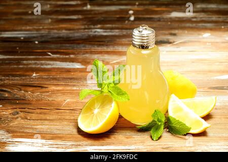 Un bicchiere a forma di bulbo di limonata fatta in casa ghiacciata alla luce del sole, fette di limone organico, lime e arancia, menta, centrifuga su tessuto di legno brunito marrone Foto Stock