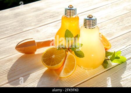 Due bicchieri a forma di bulbo, limonata fatta in casa con fette di limone e arancia matura biologica, intera e dimezzata, centrifuga, muddler, su un bianco rustico Foto Stock