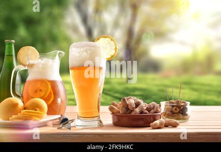 Dettaglio di un bicchiere di birra con limone e spuntini su tavola in legno in campagna. Vista frontale. Foto Stock