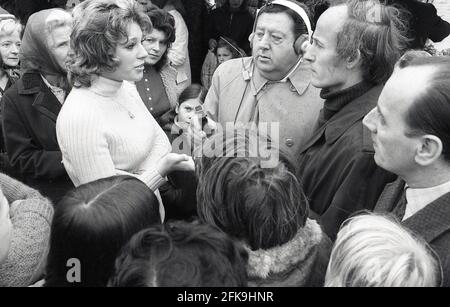 Anni '70, uomo popolare della gente, presentatore e reporter radiofonico, Monty Modlyn con le cuffie e microfono che si animano ad una donna attraente che parla, circondato da altre persone in una zona di mercato del sud di Londra, Inghilterra, Regno Unito. Nato da una famiglia ebraica di Lambeth, Modlyn era noto per il suo accento di cetney e la sua trasmissione forte stava intervistando la gente comune, una tecnica che divenne nota come 'Vox Pop'. Rivolgendosi alle persone con le parole 'Ullo darlin', il suo personaggio della classe lavoratrice dell'estremità orientale lo ha visto parlare di tutto e di tutto durante una lunga e distinta carriera di radiodiffusione. Foto Stock