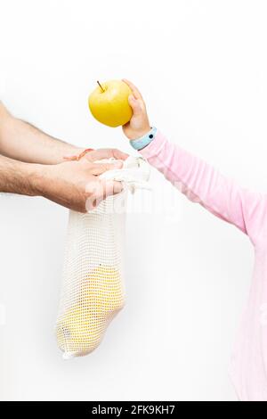 Una ragazza che mette una mela in una pezza di frutta che tiene da un maschio adulto. Sfondo bianco. Foto Stock