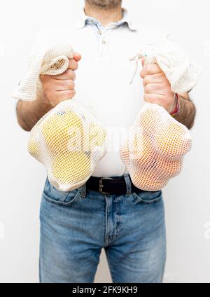 Un uomo irriconoscibile che tiene due sacchi di rete organici con mele e arance. Sfondo bianco. Foto Stock