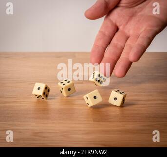 Mano che lancia cinque dadi su un tavolo di legno Foto Stock