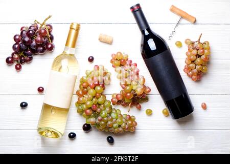 Bottiglie vintage di vino rosso e bianco con etichetta opaca bianca, cavatappi e uva, sfondo tavola in legno. Bottiglia costosa di cabernet sauvignon Concept. Foto Stock