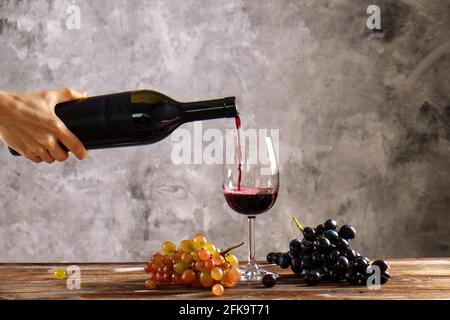 Donna con bottiglia d'annata di vino rosso. Primo piano di mano femminile giovane versando costoso cabernet Sauvignion in vetro, tavolo di legno. Bun diverso Foto Stock