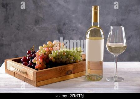 Bottiglia di vino bianco vintage con etichetta opaca in bianco, mazzo di uve diverse su tavola in legno, fondo in calcestruzzo. Costosa bottiglia di shardonnay co Foto Stock