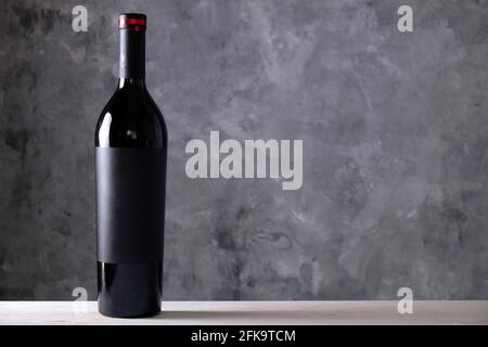 Bottiglia d'annata di vino rosso con labe nero bianco opaco su tavolo in legno, fondo parete in cemento. Bottiglia costosa di cabernet sauvignon Concept. Copia Foto Stock