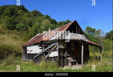 Il vecchio negozio appalachiano è chiuso e in rovina. Panca di legno siede sul portico anteriore. Il tetto in stagno è arrugginito e patchato. Foto Stock