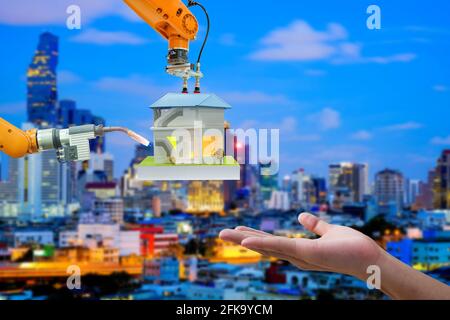 Robotica industriale in primo piano che lavora con il mockup domestico per inviare a mano umana su sfondo di colore blu offuscato del paesaggio urbano, concetto industriale 4.0 Foto Stock