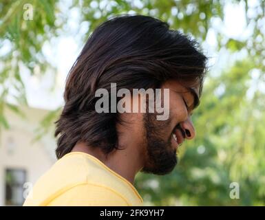Giovane bel maschio indiano bearded con lunghi capelli in piedi all'aperto e sorridendo Foto Stock