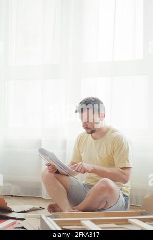 Giovane uomo attraente in una T-shirt gialla assembla i mobili Foto Stock