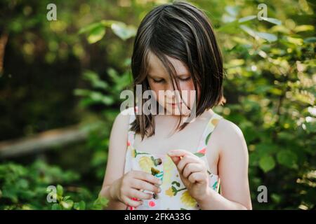 Giovane ragazza guarda un dente di leone circondato da alberi e. altro verde Foto Stock