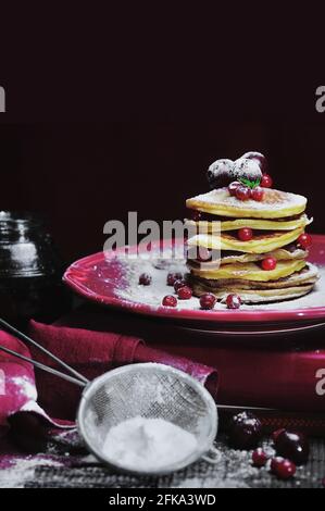 Impila di frittelle con frutti di bosco freschi e zucchero in polvere piastra rossa Foto Stock