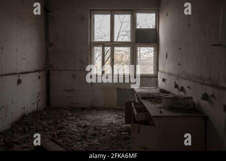 Immagine di un interno danneggiato di un edificio abbandonato con una stanza piena di polvere, rifiuti e una scrivania rimanente. Foto Stock