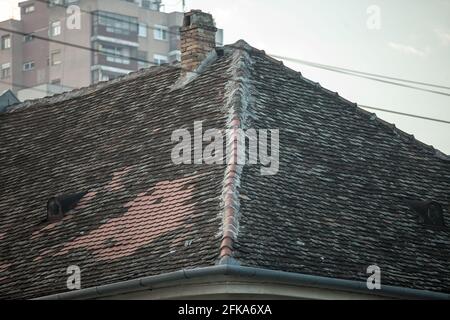 Immagine di un vecchio tetto, parzialmente riparato, ma principalmente in cattive condizioni, con piastrelle danneggiate e timonature mancanti. Foto Stock