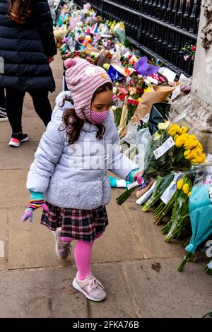 Un bambino getta fiori fuori Buckingham Palace in memoria del principe Filippo (il duca di Edimburgo) che era recentemente passato via, Londra, Regno Unito. Foto Stock