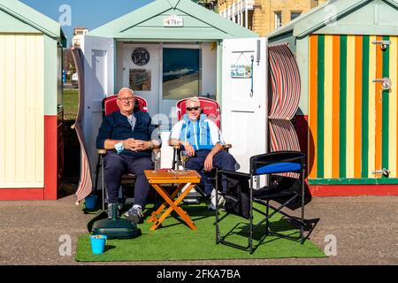 Due uomini locali che si godono il sole all'esterno DI UN rifugio sulla spiaggia di Hove Seafront, Brighton, East Sussex, Regno Unito. Foto Stock