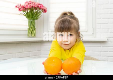 felice bambina con due tangerini. bambino tiene fuori la frutta grande in avanti Foto Stock