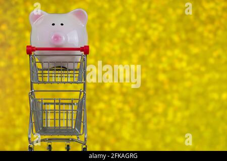 Closeup di porcellino rosa di banca in piedi su mini shopping Spingere il carrello sul copyspace giallo sfocato Bokeh sfondo Foto Stock