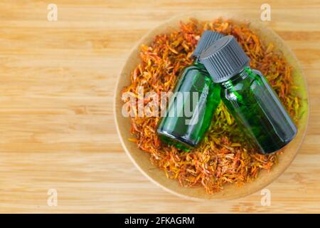 Estratto di olio concentrato puro di Safflower Essential in flacone verde ciotola di pianta di cartamo essiccata su fondo di legno con copyspace (Cartamus tinto Foto Stock