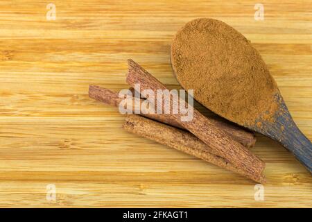 Polvere di cannella su cucchiaio di legno accanto a bastoncini di cannella fatti di corteccia interna su sfondo di legno con copyspace Foto Stock