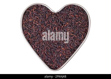 Padella di stagno a forma di cuore piena di grani di riso di Riceberry crudi in tonalità viola rossastra coltivata in Thailandia, isolata su sfondo bianco. È un betw crossbred Foto Stock
