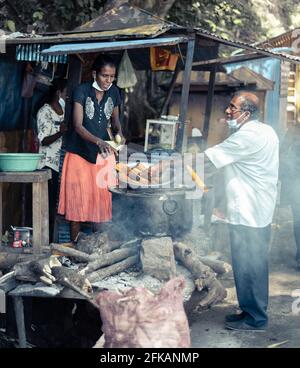 Ella, Sri Lanka - 04 15 2021: Acquisto di cibi di strada vicino Rawana Ella da un venditore di lady locale da un uomo con una maschera facciale, la vendita di deliziosi bolliti e gr Foto Stock