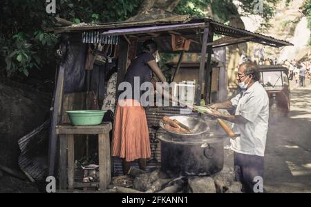 Ella, Sri Lanka - 04 15 2021: Acquisto di cibi di strada vicino Rawana Ella da un venditore di lady locale da un uomo con una maschera facciale, la vendita di deliziosi bolliti e gr Foto Stock