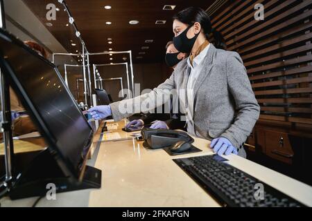 I receptionist dell'hotel seguono le precauzioni di sicurezza pandemiche Foto Stock