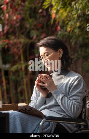 Leggere una donna anziana all'aperto in sedia a rotelle Foto Stock