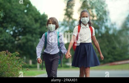 I bambini tornano a scuola. Simpatici alunni con zaini. Ragazzo e ragazza in maschere di sicurezza Foto Stock