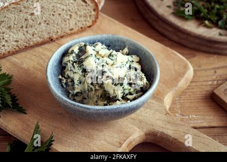 Burro di erbe fatto di nettle fresche raccolte in primavera, con un filone di pane di pasta acida sullo sfondo Foto Stock