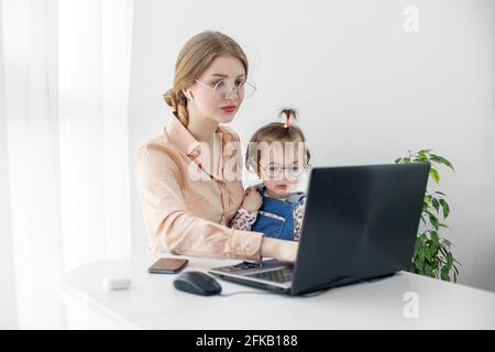 La giovane donna lavora a casa utilizzando un computer portatile. Un ragazzino è seduto tra le braccia della madre. Lavoro sul congedo di maternità. Foto Stock