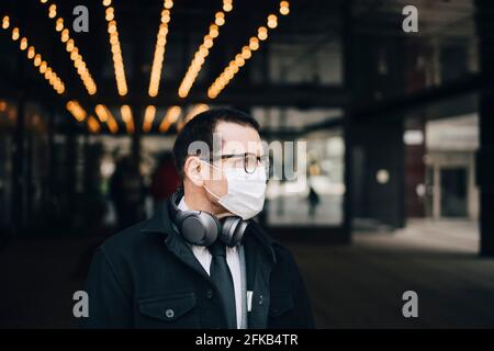 Uomo d'affari con le cuffie che guardano via durante la pandemia Foto Stock