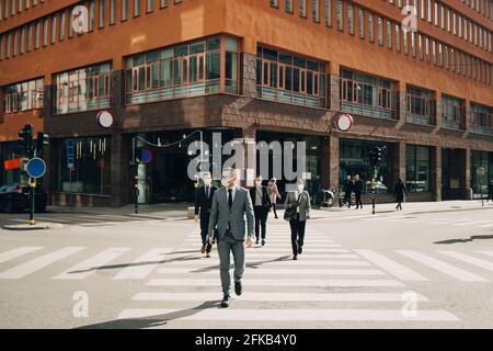 Uomini d'affari che attraversano la strada il giorno di sole durante COVID-19 Foto Stock