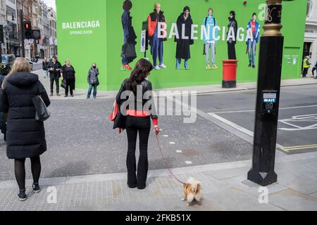Gli acquirenti attraversano la strada verso l'imbarco temporaneo per Balenciaga, uno spazio al dettaglio che sta per aprirsi a breve su Bond Street, il 27 aprile 2021, a Londra, Inghilterra. Balenciaga è una casa di moda fondata nel 1917 dallo stilista spagnolo Cristóbal Balenciaga a San Sebastián, Spagna. Foto Stock