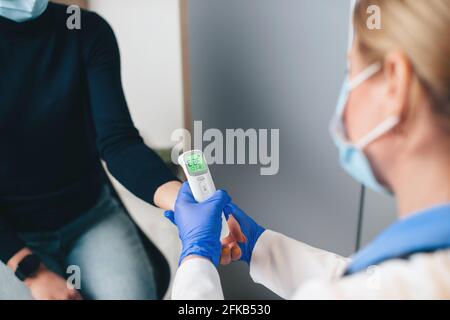 Primo piano della foto di un medico caucasico senior che usa un termometro elettronico per misurare la temperatura del paziente Foto Stock